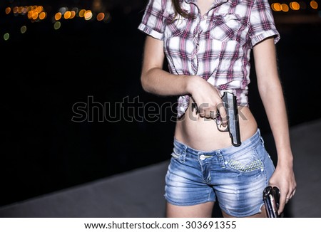 Woman\'s hand with two metal gun. Young unrecognizable girl against dark city light Sexy Female wear casual dress Empty copy space for inscription