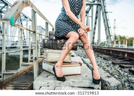 No face Unrecognizable person of Young adult caucasian girl sit on railway metal bridge construction background Cute slim woman waiting train with many big brown suitcase Female wear short black dress