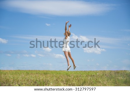 Alone blond Woman Jumping for Joy on a Grass Hill above horizon line One happy slim girl fly in a green field against blue summer sky with clouds Idea of success, growth , light, diet, luck, freedom