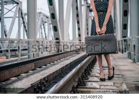 No face Unrecognizable person of Young adult caucasian girl stand on railway metal bridge construction background Cute slim woman wait train with many big brown suitcase Female wear short black dress