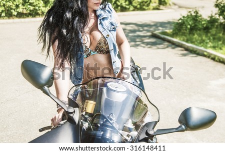 No face brunette woman sit on black sports motorcycle Very hot sexy young femme fatale girl wear denim vest. Sexy Lady against green summer bush background Empty space for inscription