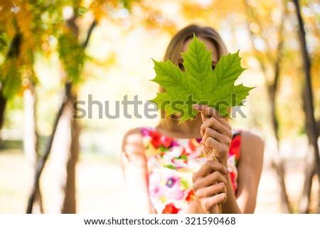 Cute Girl holding in hands green maple leaves Young adult woman wear colorful dress with flowers pattern Female stand outdoor against yellow autumn park Empty copy space for inscription