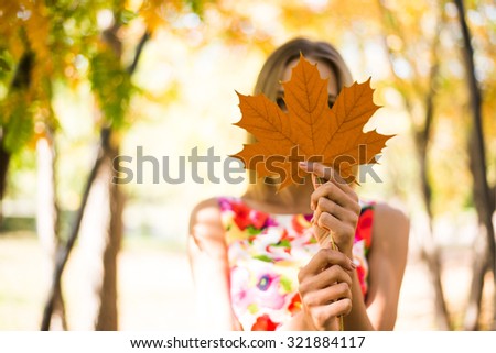 Cute Girl holding in hands green maple leaves Young adult woman wear colorful dress with flowers pattern Female stand outdoor against yellow autumn park Empty copy space for inscription