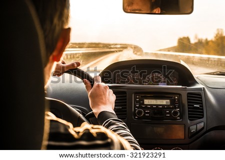 Man hand driving a car at sunset evening sky light Autumn Road between trees forest Male sit inside control volume audio system Finger lie on wheel Empty copy space for inscription