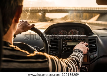 Man hand driving a car at sunset evening sky light Autumn Road between trees forest Male sit inside control volume audio system Finger lie on wheel Empty copy space for inscription