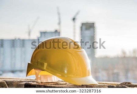 yellow plastic helmet for workers security lie on windowsill  of window frame against multistories house with construction crane at evening light background Copy space for inscription or objects