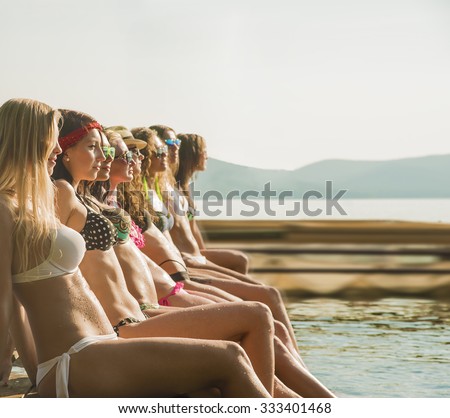 group of happy young woman feet splash water in sea and spraying at the beach on beautiful summer sunset light. Eight sexy girls playing on wooden pontoon against blue sky background Enjoy holiday