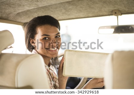african american young adult woman with smiley face sit inside retro vintage luxury white car with blank metal license plate number, nameplate, sign. Empty copy space for inscription or objects