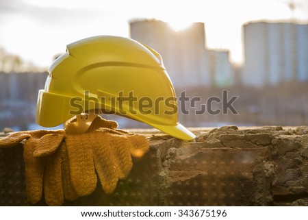 yellow plastic helmet for workers security lie on windowsill of window frame against multistories house with construction crane at evening light background Copy space for inscription or objects