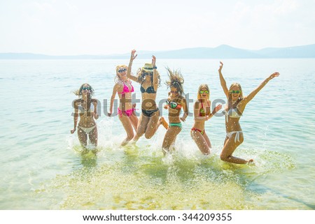 Silhouette of young group of people jumping in ocean at sunset Team of adult girl jump in water on summer beach against blue sky with clouds Water splash Hair fly in air Empty space for inscription