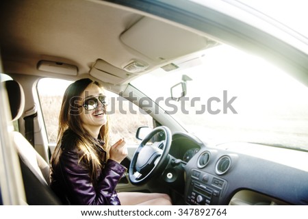 woman in car indoor keeps wheel turning around smiling looking at passengers in near seat. idea taxi driver sit against sunset rays Light shine sky Concept of exam Vehicle - second home the girl