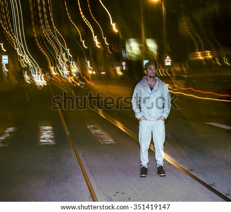 full length portrait of alone sporty young man stand on night urban asphalt road against night  city urban environment with colorful light