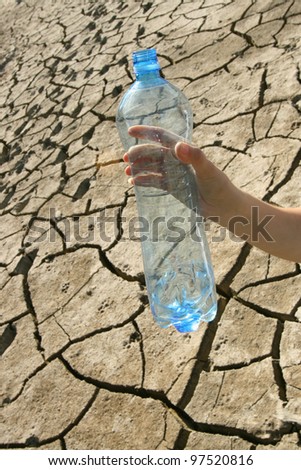 concept of of water shortage - a hand with an empty bottle on the background of dried ground