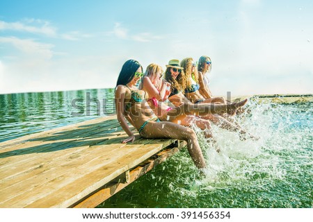 group of happy young woman feet splash water in sea and spraying at the beach on beautiful summer sunset light. Five sexy girls playing on wooden pontoon against blue sky background. Enjoy holiday