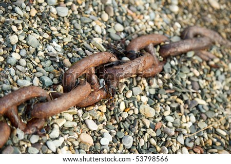 Large rusty chain in stones on beach with copy space.