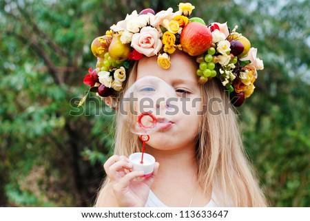 Happy Child in Summer.  Beautiful Girl with Flowers Wreath from Flowers blows Soap Bubbles. Happy Children. Healthy Kids. Spring Time.