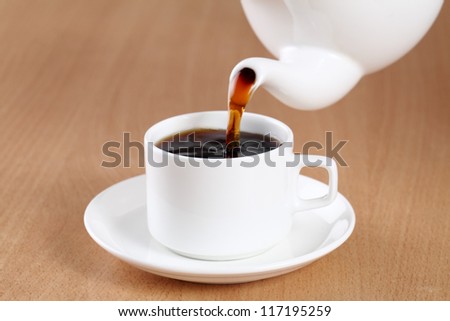 Tea being poured into tea cup on table.