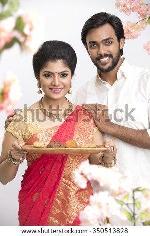 Young happy south Indian couple holding cookies and sweets for Indian festival on white.