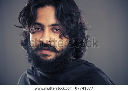 Indian young man with long hair on grey background.