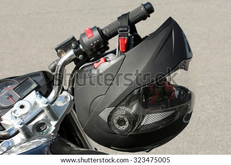 Motorcyclist\'s crash-helmet hanging on the handle of a motorcycle.