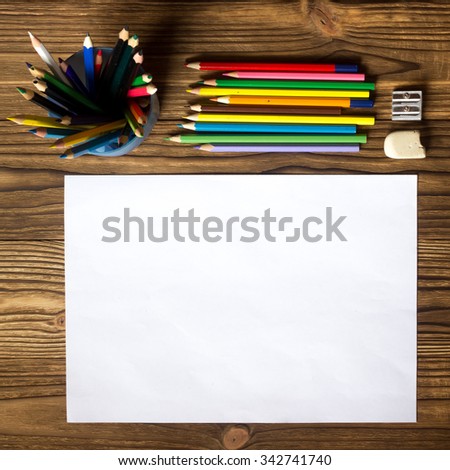 white sheet of drawing and drawing close to the set of colored pencils of different colors, and a set of drawing on the wooden background