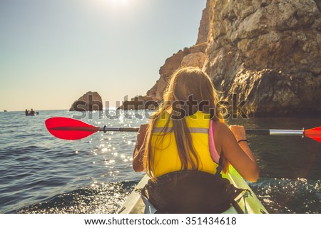 Young blonde woman kayaking alone  in the sea near mountains and holding oar