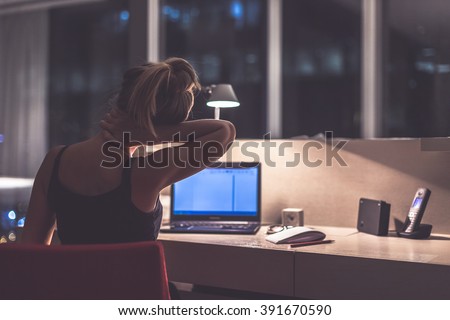 Young exhausted,depressed,concentrated woman sitting in her room or office with french windows  in the dark at the lamp.Studies late at night.Staying up late. Overworking. Feeling pain in the neck