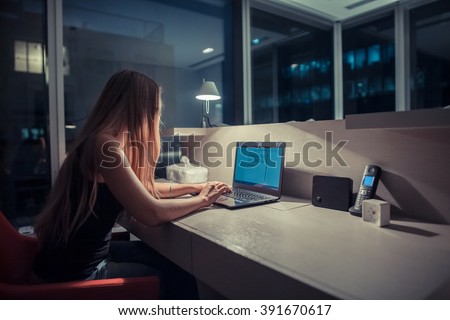 Young exhausted,depressed,concentrated woman sitting in her room or office with french windows  in the dark at the lamp.Studies late at night.Staying up late. Overworking.