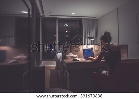 Young exhausted,depressed,concentrated woman sitting in her room or office with french windows  in the dark at the lamp.Studies late at night.Staying up late. Overworking.