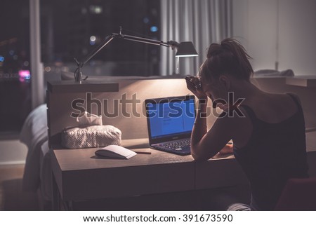 Young exhausted,depressed,concentrated woman sitting in her room or office with french windows in the dark.Studies late at night.Staying up late. Overworking.Feeling under pressure and headache