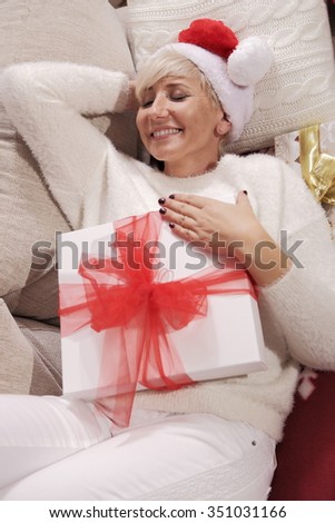 Mature woman lying on a couch in a festive dress with a gift. Beautiful view of a happy woman. The charming picture.