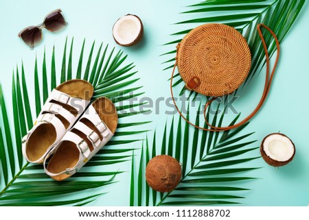 Round rattan bag, coconut, birkenstocks, palm branches, sunglasses on blue background. Banner. Top view with copy space. Trendy bamboo bag and shoes. Summer fashion flat lay. Trip, vacation concept.