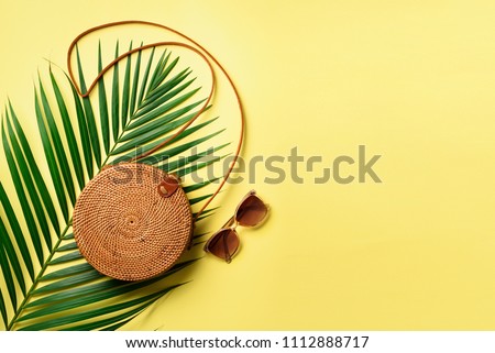 Round rattan bag, sunglasses on yellow background. Banner. Top view with copy space. Trendy bamboo bag and white shoes. Summer fashion flat lay. Trip, vacation concept.