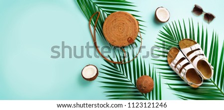 Round rattan bag, coconut, birkenstocks, palm branches, sunglasses on blue background. Banner. Top view with copy space. Trendy bamboo bag and shoes. Summer fashion flat lay. Trip, vacation concept.
