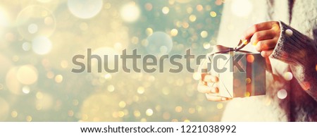 Shimmer background with snow, light bokeh. Woman hands opening gift box. Christmas, new year, birthday concept. Banner, copy space.