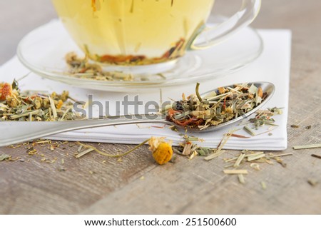 Dry herbs in a spoon and herbal tea on a background
