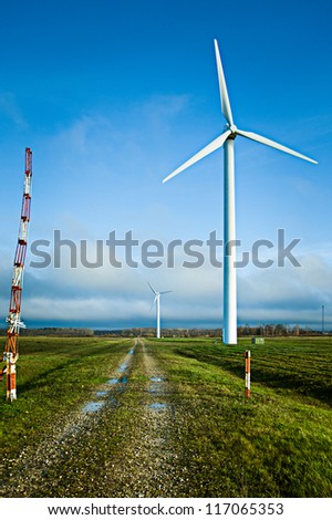 A wind electric generator in field at the rural road.