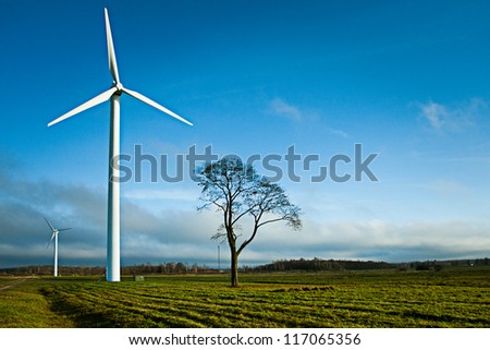 Two wind electric generators in field with alone tree.