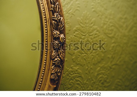 Oval mirror fragment with gold frame on the green wall