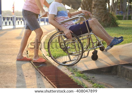 Mother helping her son on wheelchair up the ramp in the park with sunset in background, warm filter