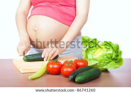 Pregnancy and nutrition - pregnant woman with vegetables on desk, isolated