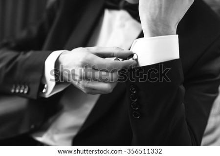 Confident man buttons cufflinks. Cufflinks closeup. Men\'s suit, tuxedo.