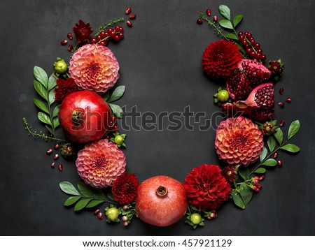 Red pomegranates and dahlias form a dramatic floral arrangement on a dark textured background for Rosh Hashanah the Jewish New Year