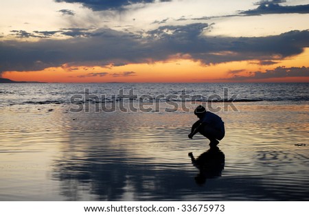 A man looking into his reflection during a sunset.