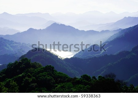 mountains surround lake with light fog. The lake surface reflect sunshine.