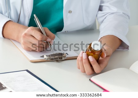 Close-up of doctor\'s hands writing prescription and holding bottle with pills. Healthcare, medical and pharmacy concept.