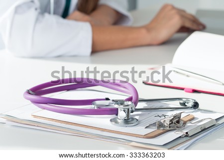 Stethoscope lying on pad with prescription form with female doctor working at background. Medicine doctor working place. Healthcare, medical and pharmacy concept. Copyspace