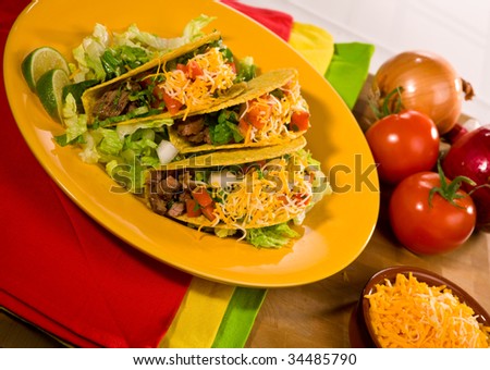 A plate of freshly prepared beef tacos with tomato, freshly grated cheese, lettuce and sour cream.