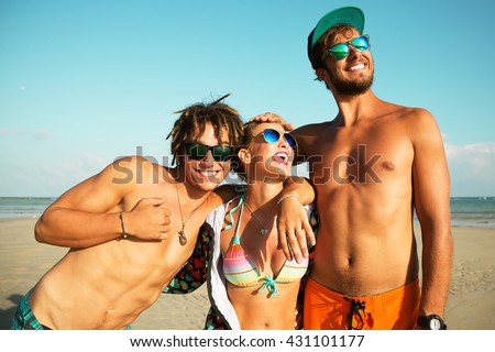 Summer lifestyle portrait of company of young cheerful best friends on the tropical beach. Smiling, having fun and posing on the water. Wearing stylish sunglasses, bright shorts and  t-shirt. Surf