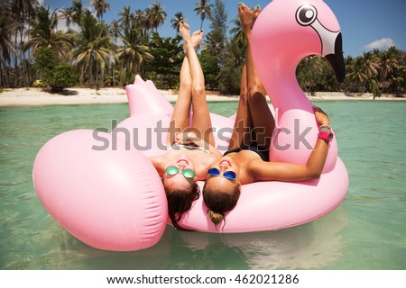 Summer lifestyle portrait of two pretty girls friends having fun on air mattress in the ocean. Wearing bikini and mirrored sunglasses. Smiling and doing yoga. Positive emotions, bright colors